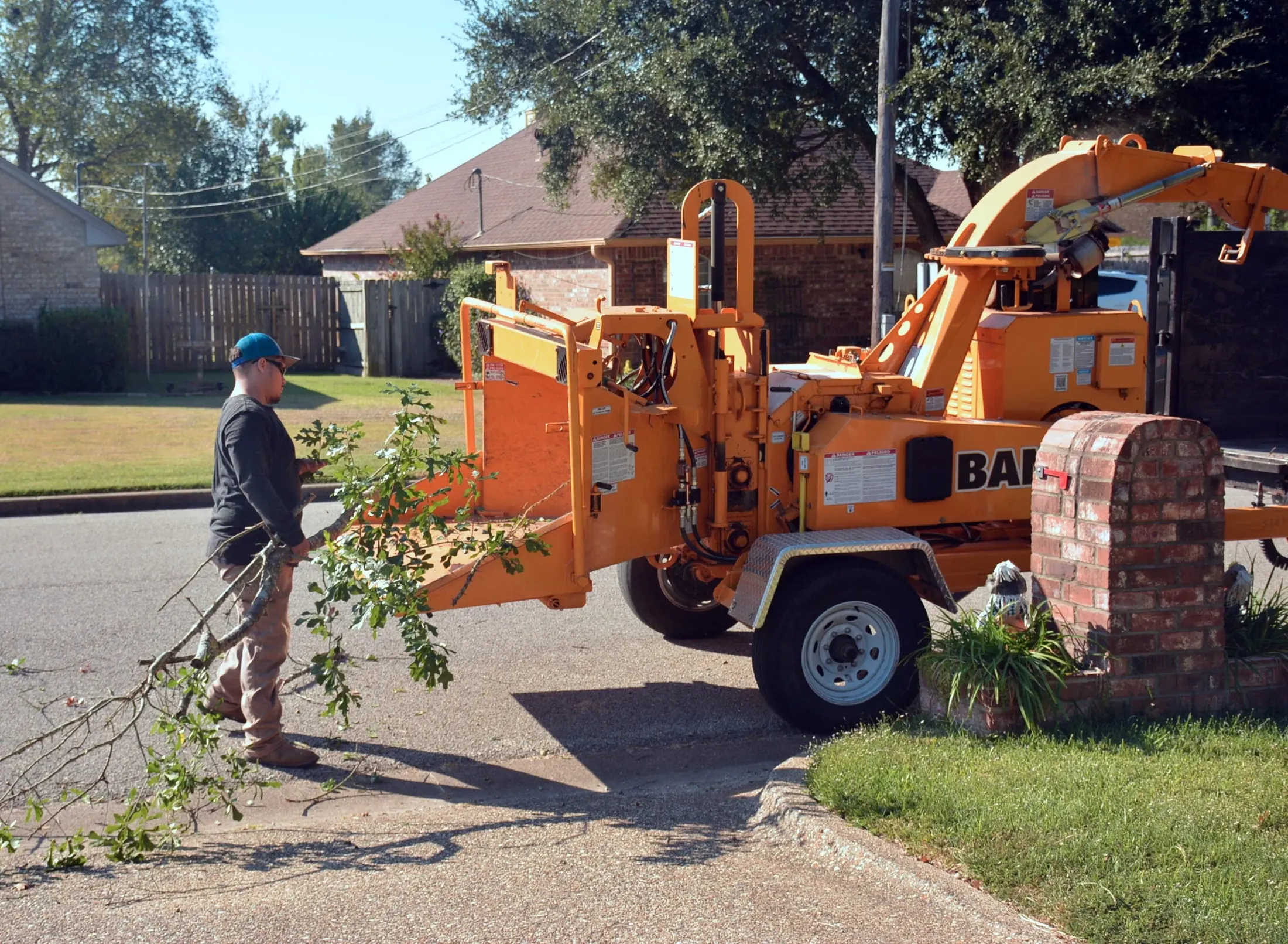 Tree service crew feeding branches into a wood chipper in a residential driveway